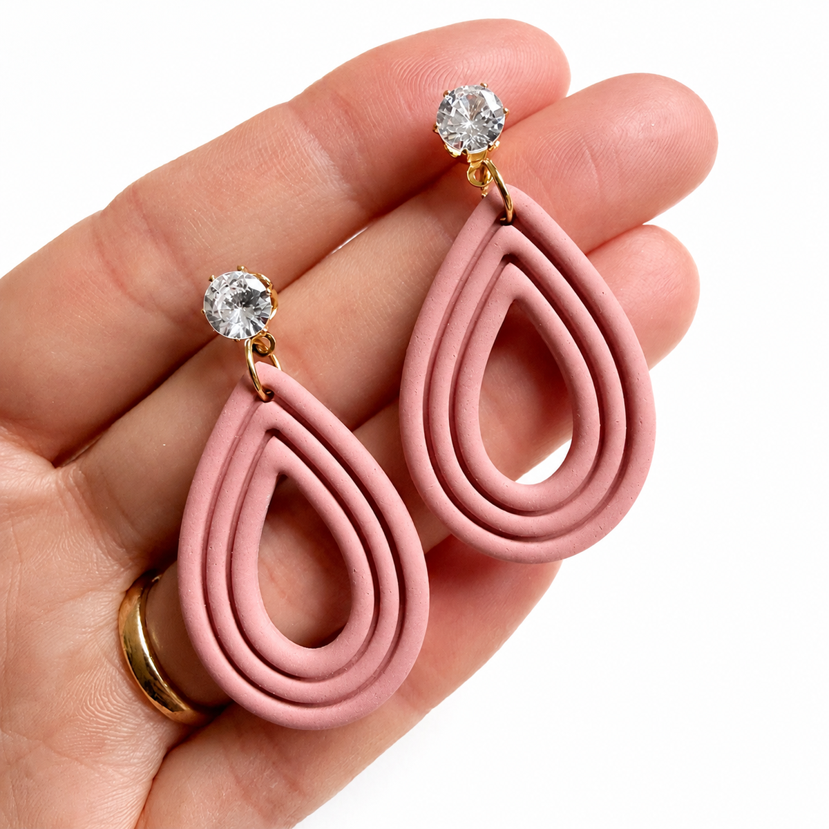 Amelie cutter, roze druppelvormige polymeerklei oorbellen met zirconia oorstekers op hand