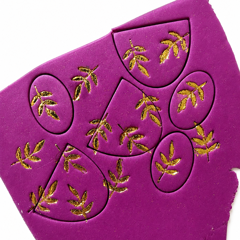 Paarse slap polymeerklei met gouden bladstempels erin gedrukt om zelf oorbellen te maken.