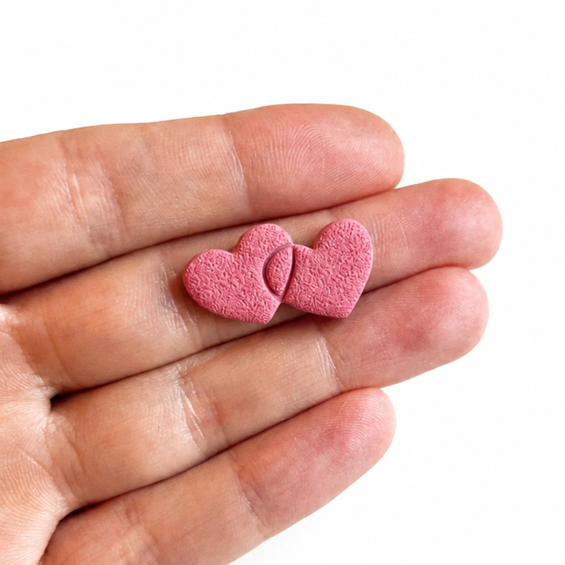 Hartjes in elkaar cutter, roze hartvormige polymeerklei oorbel op hand
