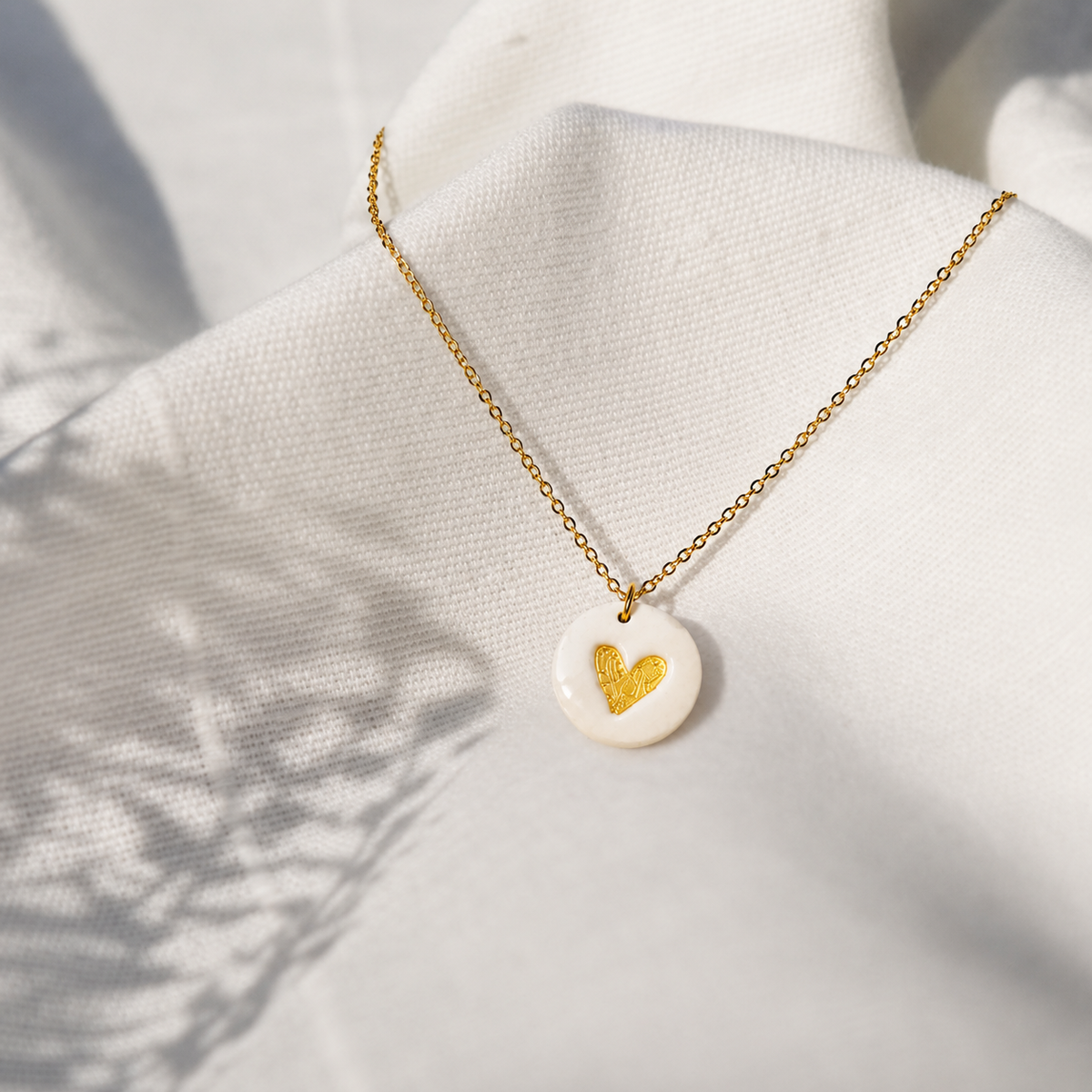 Gouden ketting met witte ronde hanger uit polymeerklei, versierd met gouden hartjes aangebracht met micapoeder.