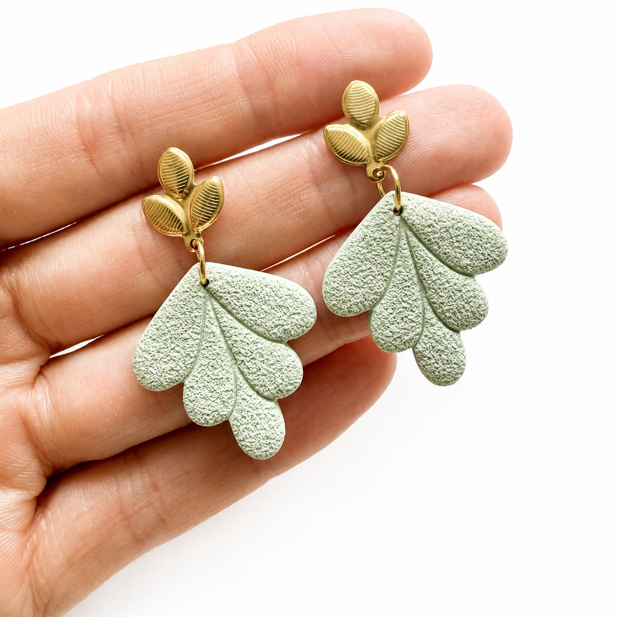 Groene bladvormige polymeerklei oorbellen op hand, afgewerkt met oorstekers blad goud
