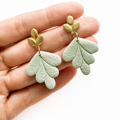 Groene bladvormige polymeerklei oorbellen op hand, afgewerkt met oorstekers blad goud