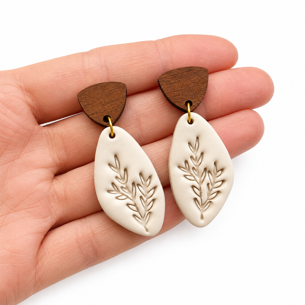 Beige polymeerklei oorbellen afgewerkt met de blad stempel en houten oorstekers op hand